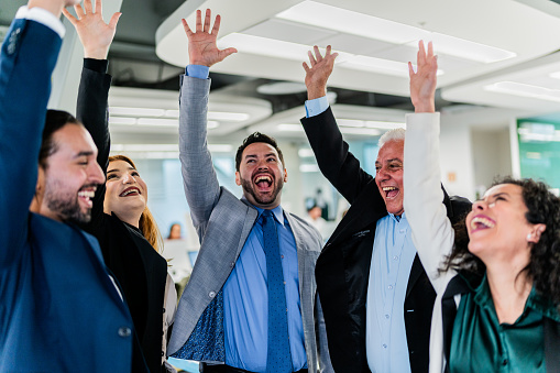 Coworkers celebrating with arms raised on the office