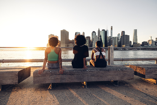 Three friends enjoying a cool sunset in New York looking at Downtown skyline from Brooklyn.