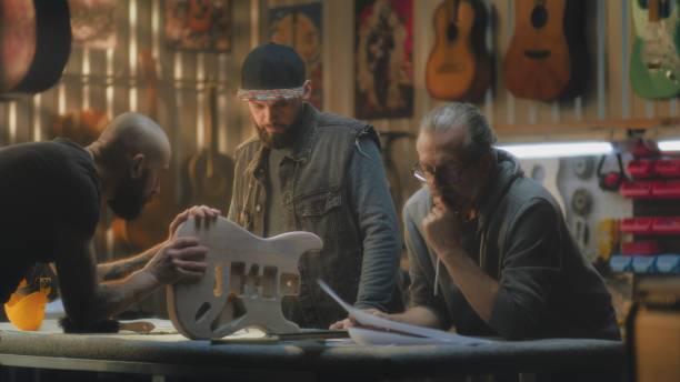 istock Tattooed craftsman holds guitar body and talks with colleagues 2028331859