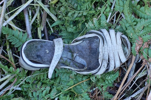 one old torn dirty white gray leather sandal stands in the green grass on the street