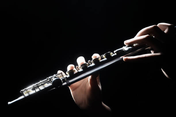 The woman's close-up hand movements on the flute create a beautiful sound during her solo performance in the classical music concert.