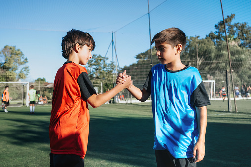 side view on two boys from opponent teams shaking hands after match on pitch