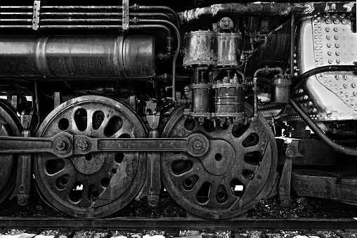 Old vintage steam locomotive wheels detail in black and white close up. The iron driving wheels are powered by the locomotive's pistons.