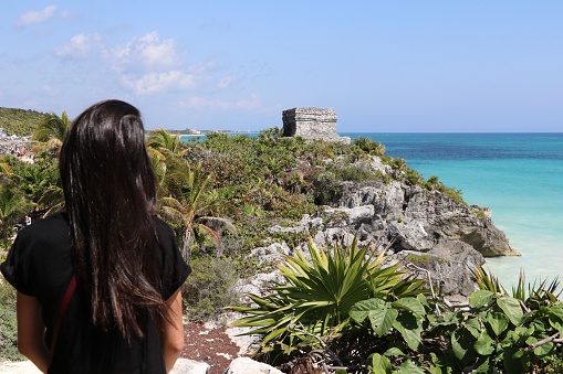 A young woman looks at the beautiful archaeological site of Tulum in Mexico