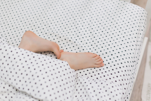 Young boy bare feet in bed under blanket