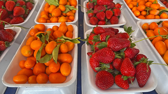 Strawberries and kumquats sold on plastic plates at the market stall.