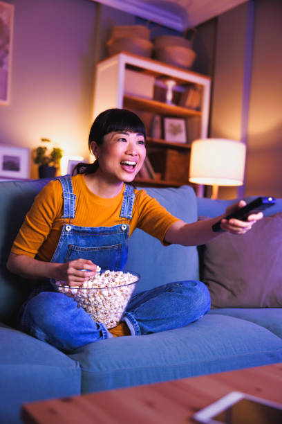 istock Woman turning on TV using remote control relaxing at home late at night 2028404082