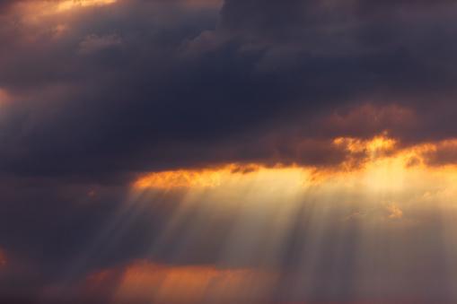 Background of the awe-inspiring beauty of a dramatic sunset sky as sunrays pierce through ominous black thunderclouds, illuminating rare orange clouds in a mesmerizing display of contrast. This striking scene captures the dynamic interplay of light and darkness, evoking a sense of both wonder and foreboding. Perfect as a standalone sky background for various creative projects, this image embodies the raw power and majesty of nature's fury.