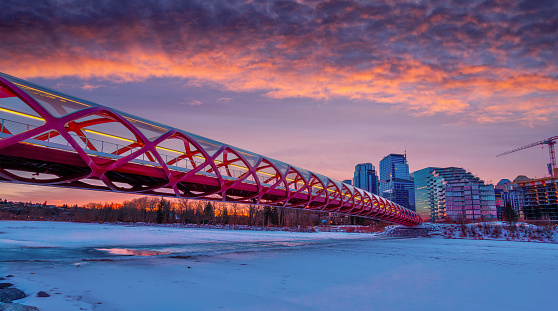 Golden sunrise in Calgary downtown with landmark Peace Bridge over the frozen and snow-covered Bow River in the Winter.