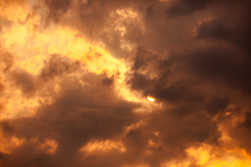 The sky background of nature's forces as rare orange clouds dominate the sky, juxtaposed against a menacing black cloud cover during sunset. This wild-looking weather system is illuminated with a golden hue, creating an abstract background texture that embodies the raw power and beauty of an untamed storm. Experience the breathtaking intensity of nature's spectacle in this captivating scene