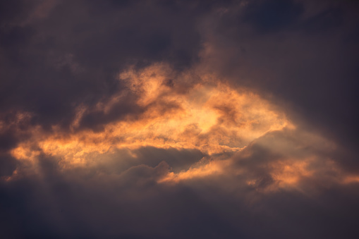 Background of the awe-inspiring beauty of a dramatic sunset sky as sunrays pierce through ominous black thunderclouds, illuminating rare orange clouds in a mesmerizing display of contrast. This striking scene captures the dynamic interplay of light and darkness, evoking a sense of both wonder and foreboding. Perfect as a standalone sky background for various creative projects, this image embodies the raw power and majesty of nature's fury.