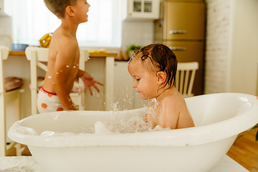 Little boy bathing his baby brother in a bath tub