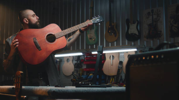 istock Male craftsman plays acoustic guitar, sets up strings 2028452288