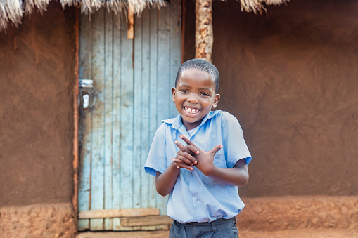 portrait of single village african child in school uniform standing in front of a hut