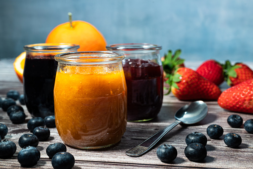 Homemade orange marmalade, assortment of homemade jams in glass jars. Front view, seasonal fruit jam, oranges, strawberries and blueberries.
