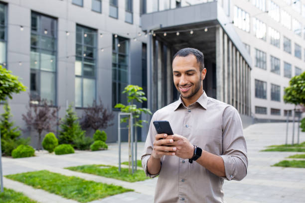 istock Smiling young hispanic male student using phone, typing message, checking and reading news, walking outside university campus 2028487789