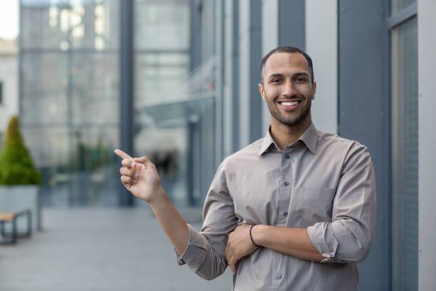 istock Handsome latino man with short haircut pointing with finger aside at empty space while smiling toothy at camera. Successful entrepreneur advising and praising new service for business consulting 2028494718