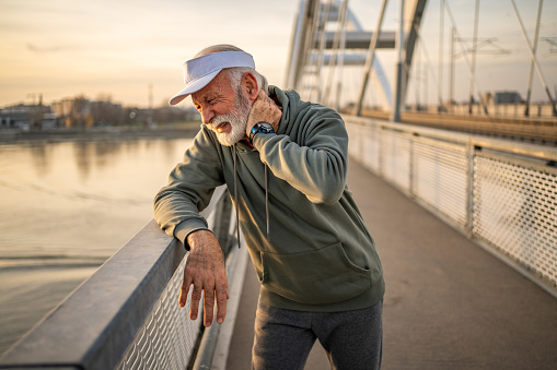 Senior Caucasian athlete has neck pain while running outdoors on a bridge