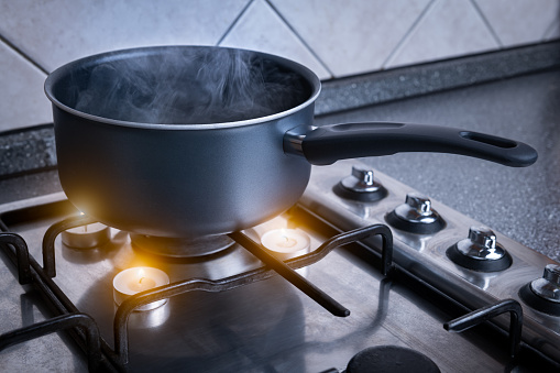 Funny concept of replacing gas with candles. Black pot with boiling water on a stove.
