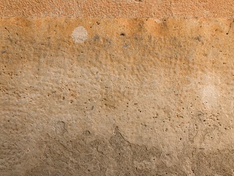 Horizontal closeup photo of an old, weathered, discoloured, beige and ochre coloured stucco rendered wall of a house in the old centre of Aix-en-Provence, south of France.