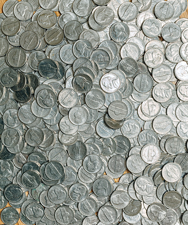 A scattered heap of USA nickel five cent coins spread out on a flat surface shot from directly above.