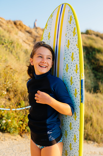 Sweet teenage girl posing together with her surfboard , walking to the beach with wet suit