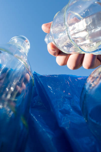 istock Man leaving a glass bottle in a blue recycling bin 2028617983