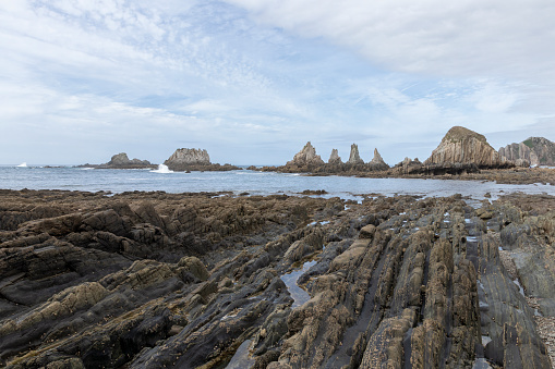 serene coastal landscape with jagged, seaweed-covered rocks jutting out of a calm sea under a partly cloudy sky