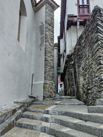 narrow, stone-paved street with steps, flanked by white buildings and a stone wall, exuding an old-world charm