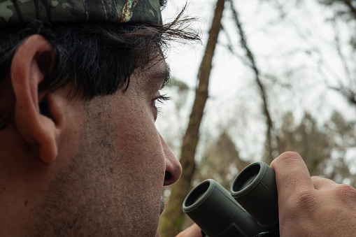 In this captivating close-up, a forest ranger stands as the guardian of the woods, attentively scanning with binoculars. His piercing gaze penetrates through the forest canopy, remaining ever vigilant to detect any signs of danger or intrusion. As a custodian of nature, his presence embodies dedication and commitment to preserving the natural environment. This image conveys the vital importance of supervision and care in the conservation of our precious forests