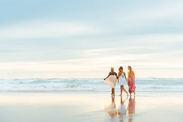 multiracial group of three friends walking together along the seashore during a summer trip. friendship and unity. women on the beach.