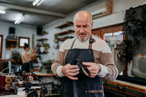 Senior man in his leather workshop with his coworkers checking belts