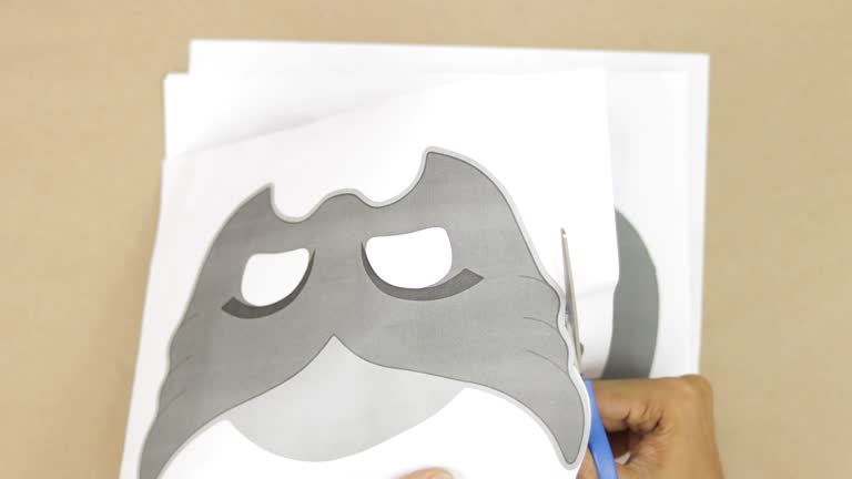 Hands cutting out printed images of childrenss masks for carnival, making molds