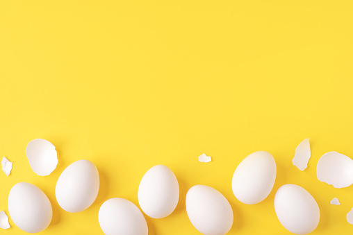 Minimalistic Easter background. White Easter eggs and shells on a bright yellow background. Card with a place for text. Top view.