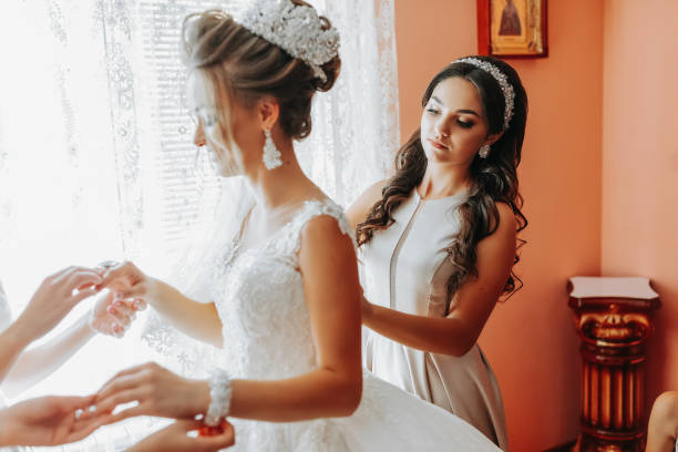 istock bride's girlfriend prepares the bride for her wedding day. The bride's girlfriend helps secure the bride's wedding dress before the ceremony. 2028990078