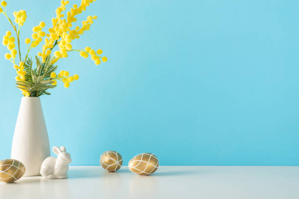 istock Easter celebration in the kitchen, captured from the side view, displaying a table with lavish gold eggs, a lovely rabbit statuette, and a mimosa vase, on a soft blue wall 2028992833