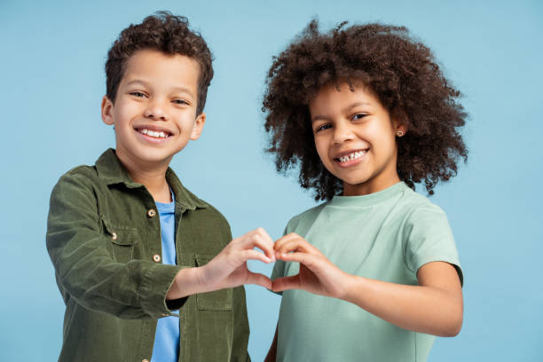 Smiling African American boy and girl positive sister and brother gesturing showing heart with hands Smiling African American boy and girl, positive sister and brother gesturing, showing heart with hands looking at camera isolated on blue background. Concept of love, family cute boy show love symbol hand stock pictures, royalty-free photos & images