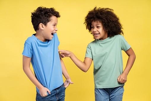 Portrait of happy, smiling African American children, beautiful brother and sister fooling around together, standing isolated on yellow background. Concept of fun, family, childhood