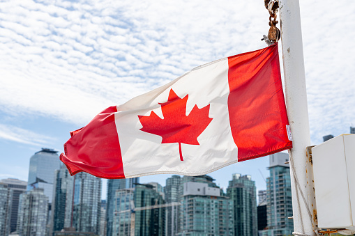 A Canadian flag flapping in the wind with the Vancouver, British Columbia skyline in the background.