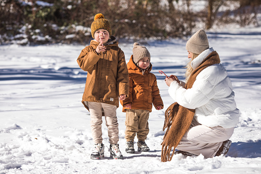 Winter weekend. Mother and two sons  in warm winterwear walking  while having fun in winter forest among trees