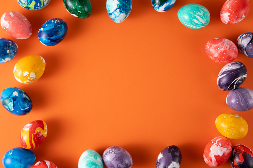 Colorfull close up of a still life of different purple Easter eggs in a pink feather nest with almond blossoms and a metallic colored Easter bunny shape on a rustic wooden background. Color editing with added grain. Very selective and soft focus. Part of a series.