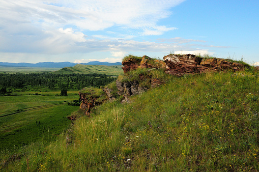 Unusual layered stone formations on top of a hill overlooking an endless picturesque valley on a warm summer day. Mountain range Chests, Khakassia, Siberia, Russia.