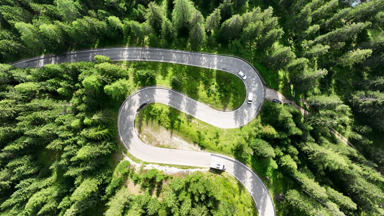 Camper van driving on snake road in forestry mountains, top down view