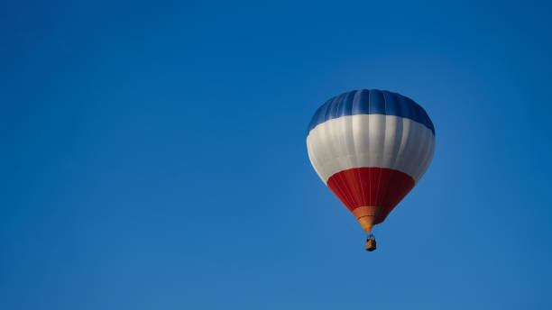 A red white and blue hot air balloon with other hot air balloons in the background.