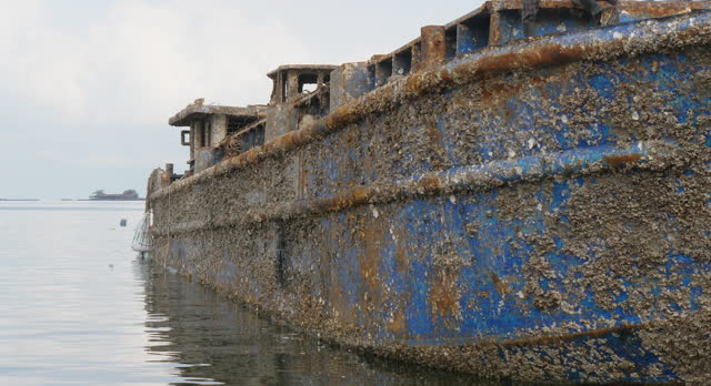 close up of the boat is heavily rusted, and barnacles and other marine life are visible clinging to its hull.