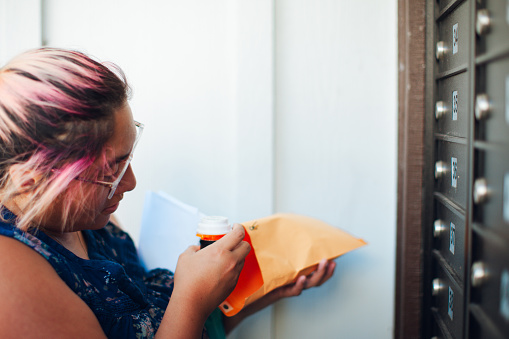 A hispanic woman opens her mail box to receive medicine sent by mail.