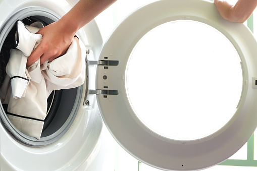 A woman opens the front door of a washing machine and puts clothes into the washing machine to clean and disinfect. Clean and healthy concept