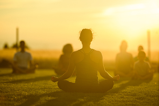 Rear view of an Eurasian woman instructing a group of children and adults in meditation and calming breath work following a yoga workout at a public park in Oregon.