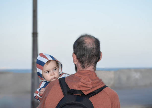 Baby boy looking over father's shoulder while daddy holding him, outdoor