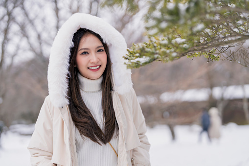 Attractive Asian traveller female woman enjoy walking carefree with winter coat speding vacation time in snow garden freshness cheerful enjoy travel concept